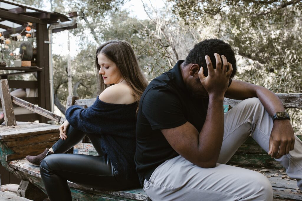 A man and woman sitting on a bench in a wooded area.