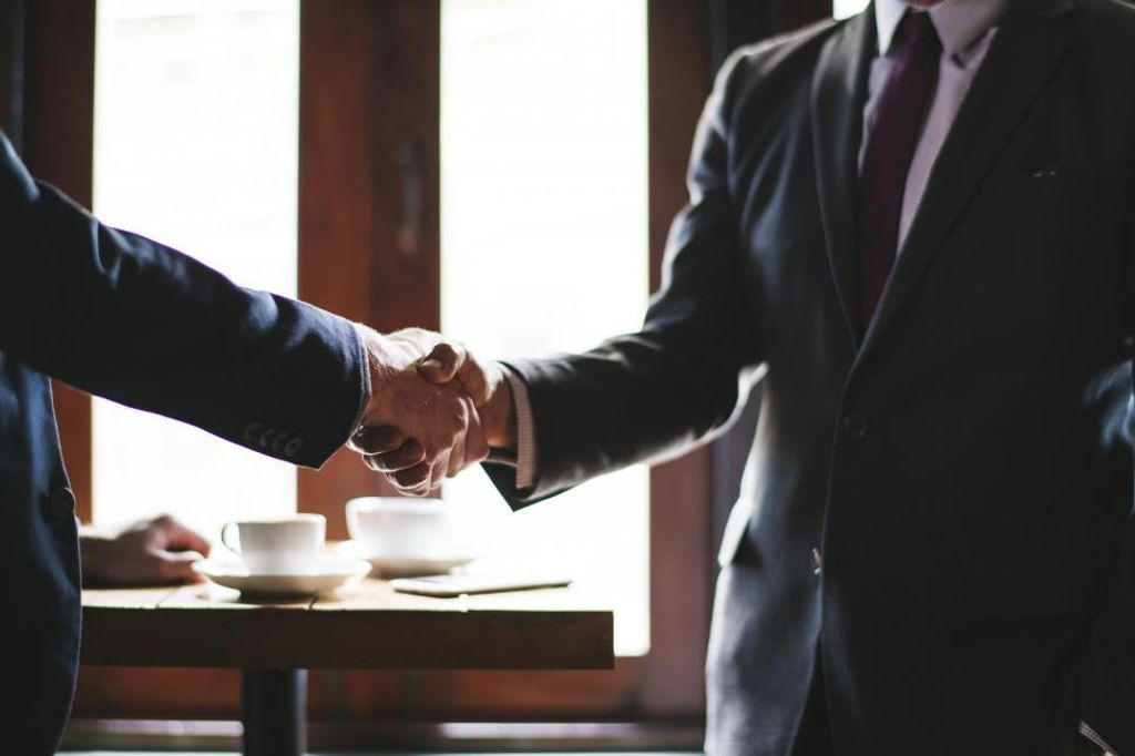 Tips for Staying Motivated as a Writer -- Accountability Partner -- Two businessmen shaking hands in front of a table.