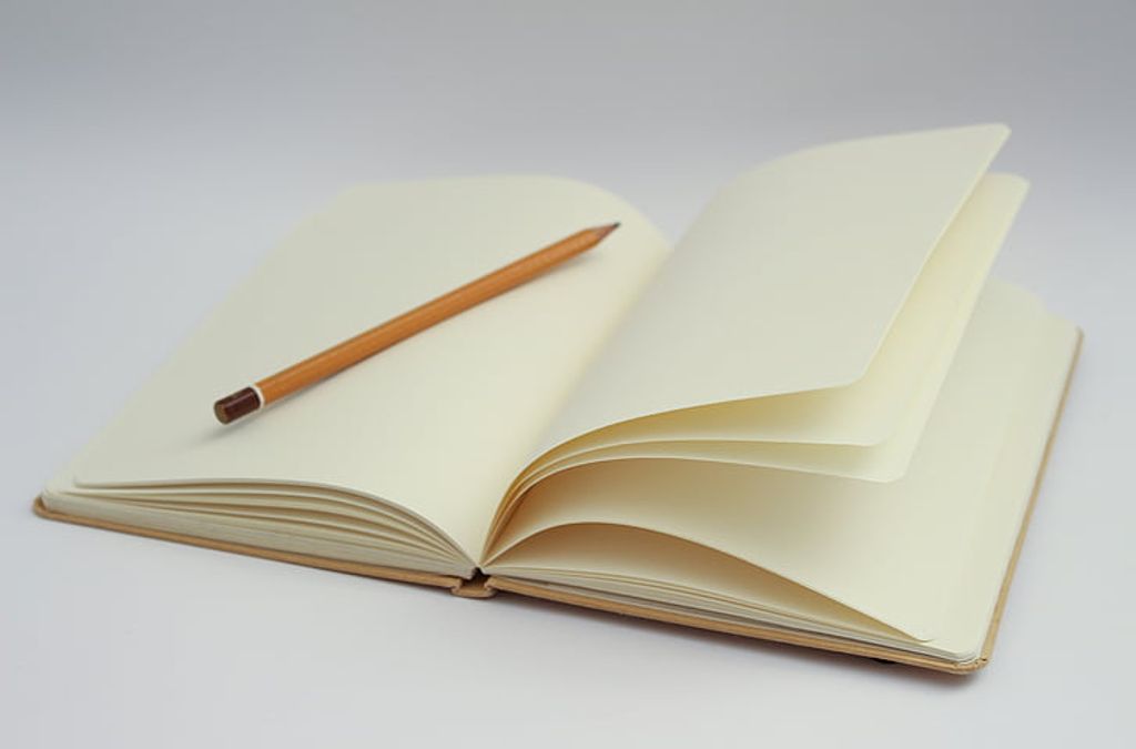 Tips for Staying Motivated as a Writer -- Writing Prompts -- An open notebook with a pencil on a white surface.